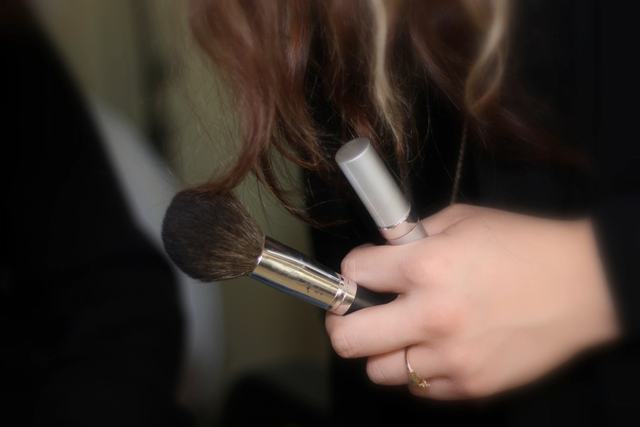 Handen houden een poederkwast en een lippenstift vast